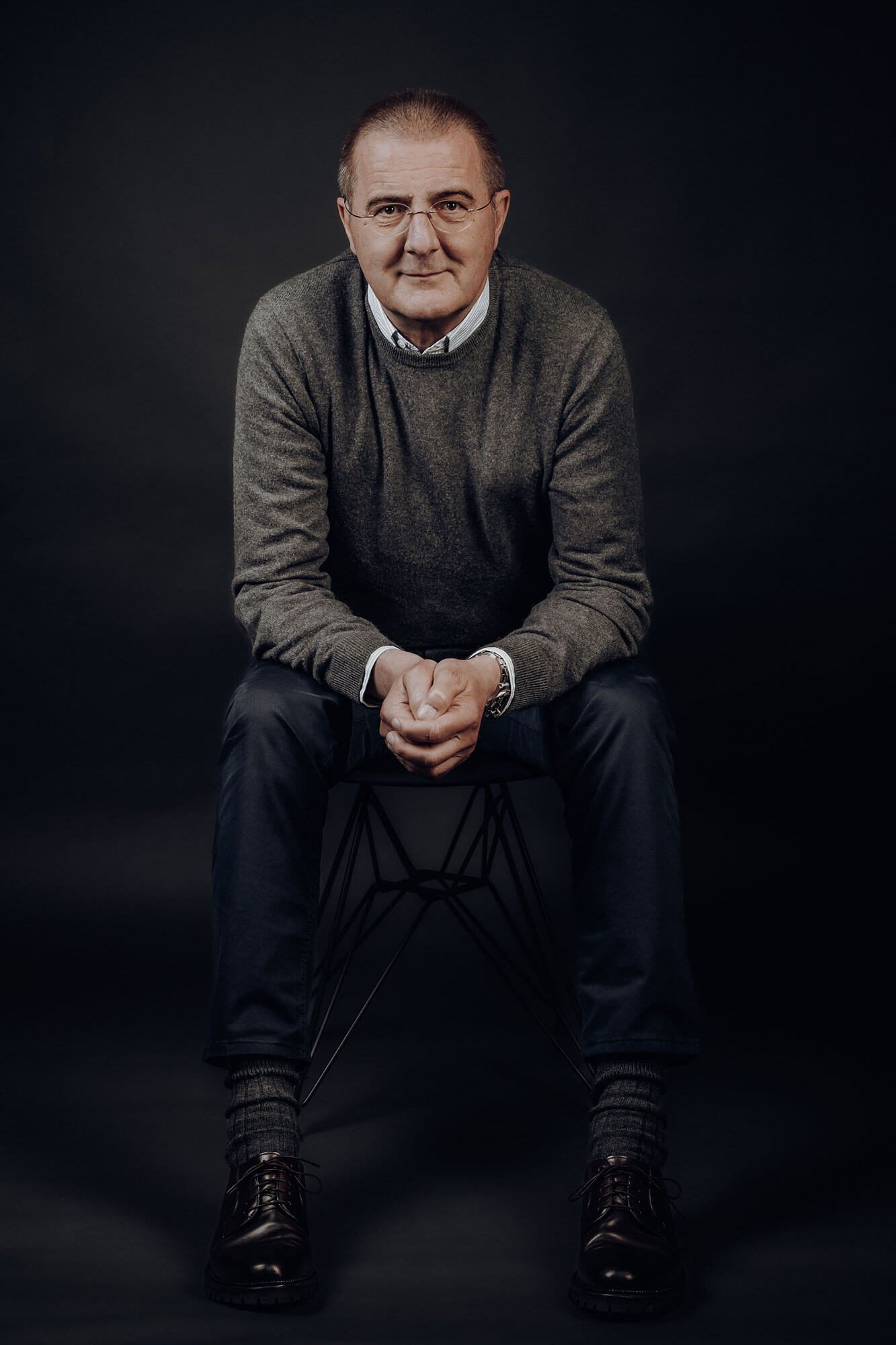 Der Geschäftsführer sitzt lächelnd auf einem Stuhl, trägt einen grauen Pullover und Jeans.