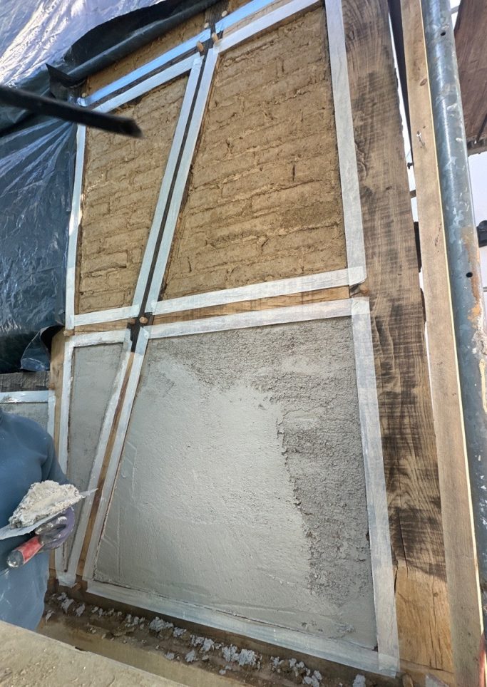 Auftragen des Putzes auf die neue Lehmstein-Ausfachung Handwerker trägt mit einer Kelle historischen Grundputz auf die Lehmsteine einer Fachwerkfassade auf.