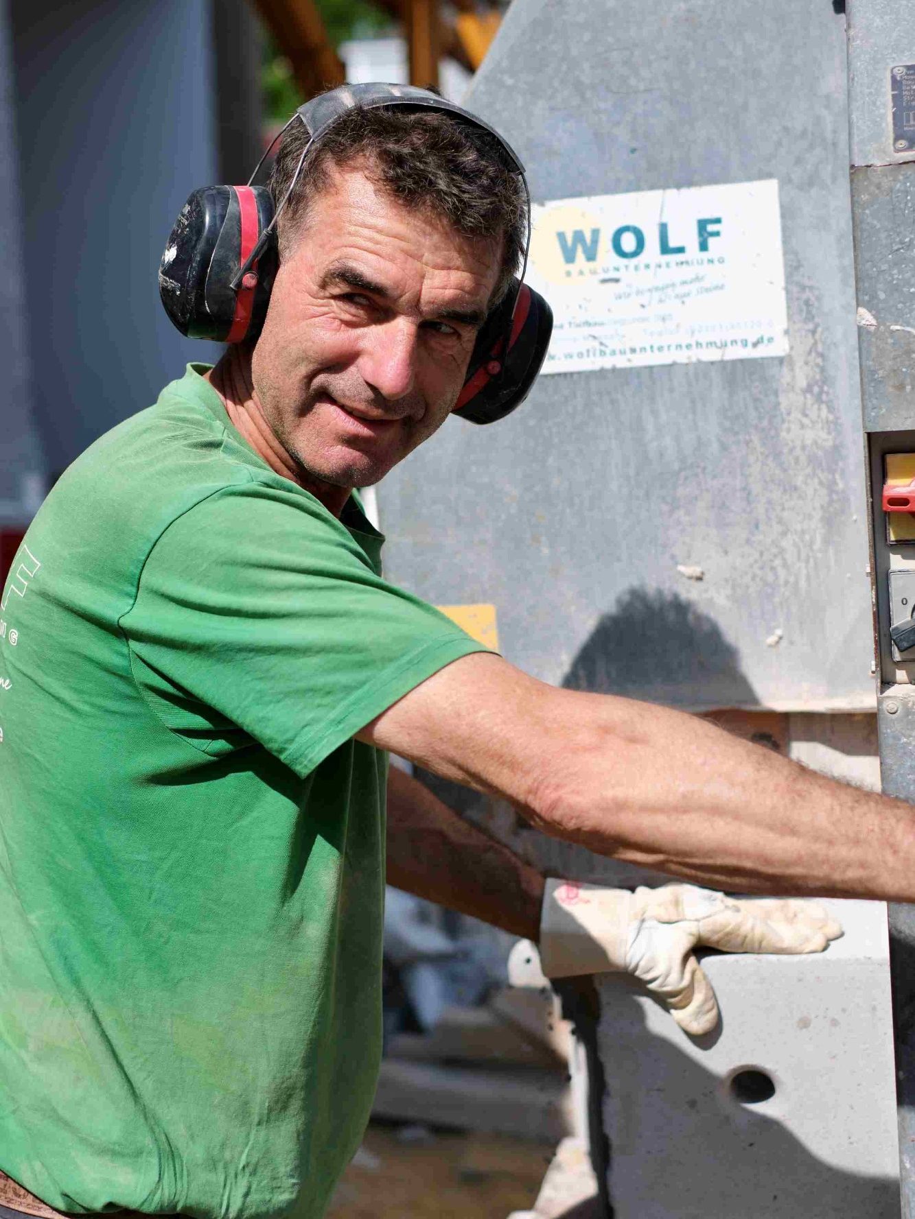Mann in grüner T-Shirt mit Kelle, leicht bekleidet und mit Bauarbeiter-Aussehen.