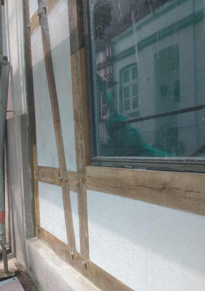 Fertiggestellte Fachwerksanierung nach denkmalpflegerischen Standards Fertig sanierte und gestrichene Fachwerkfassade mit hellen Gefachen neben historischen Holzbalken und einem Fenster.