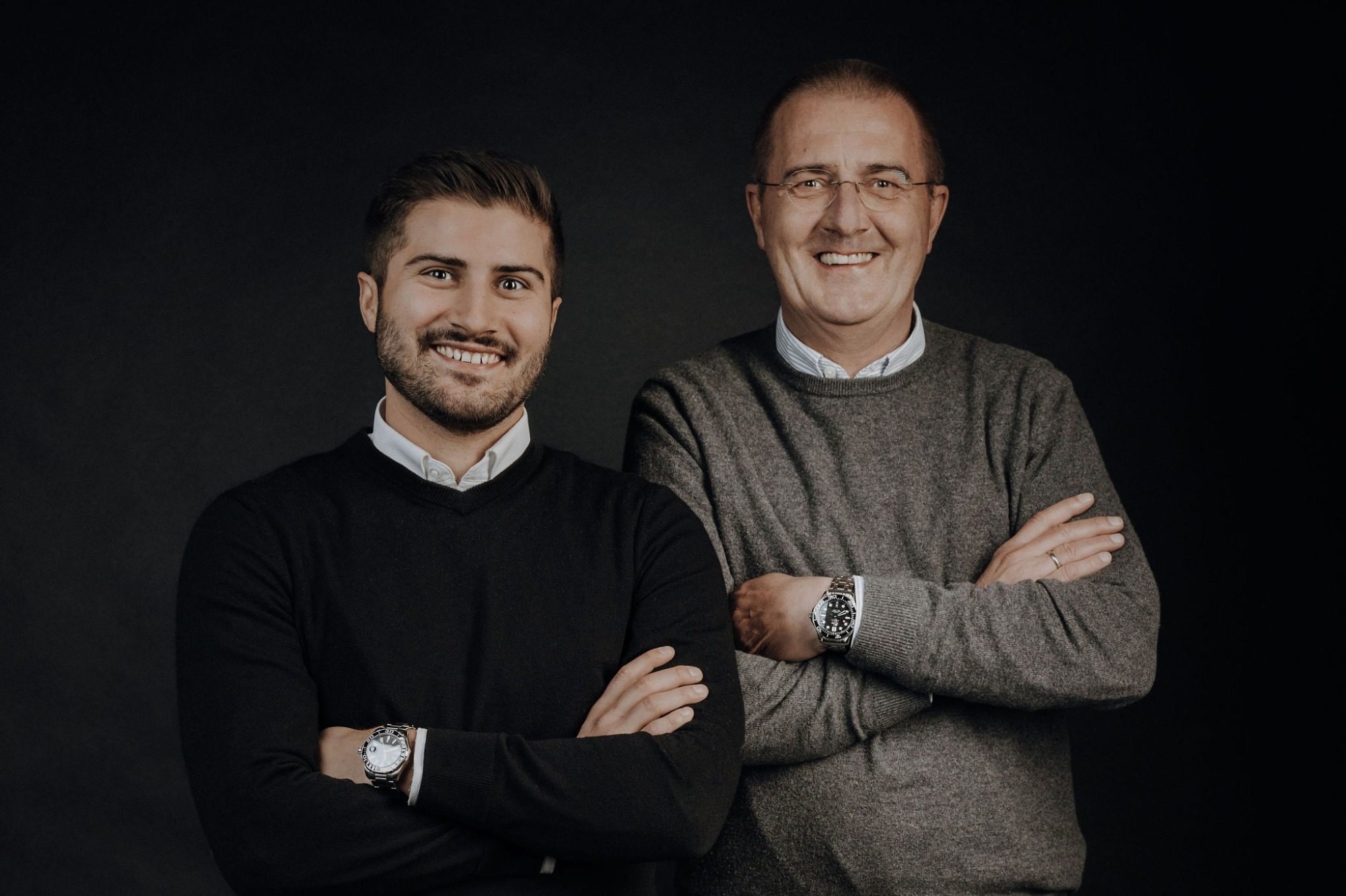 Vater und Sohn mit verschränkten Armen, einer in schwarzem Pullover, der andere in grauem Pullover.