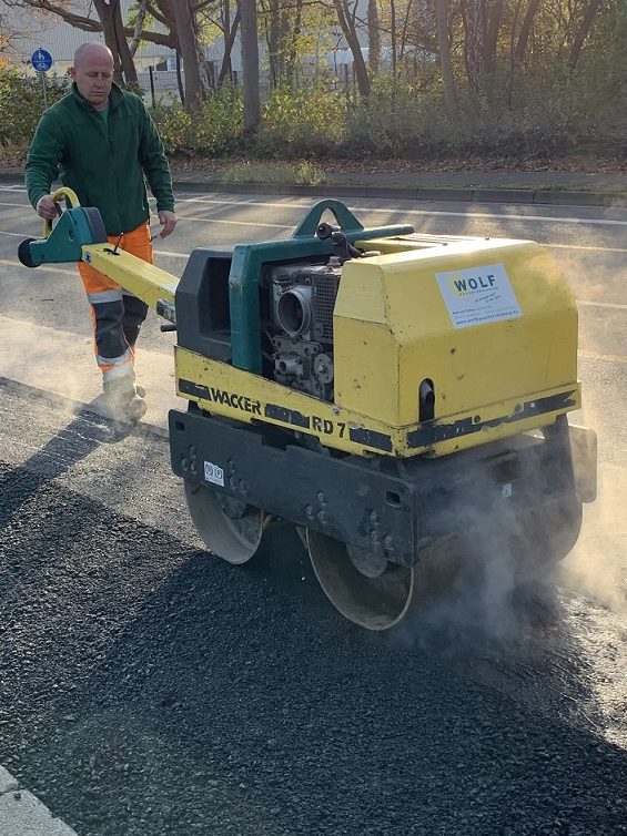 Asphalt- und Oberflächensanierung: Verdichtung mit der Tandemwalze Ein Mitarbeiter bedient eine handgeführte Walze zur Verdichtung einer frischen Asphalt-Deckschicht